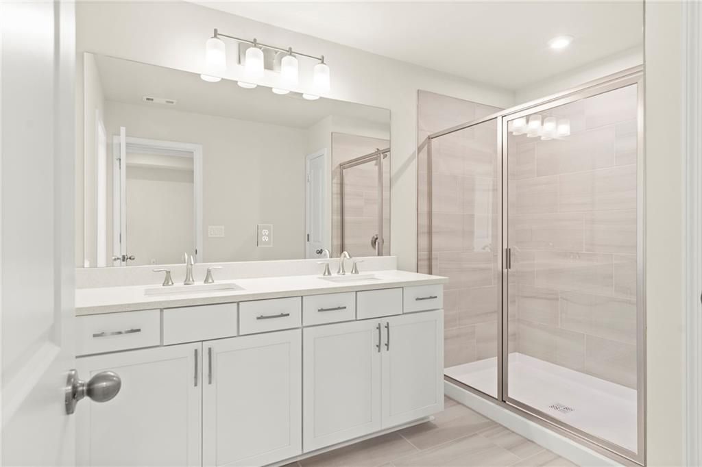 Modern master bathroom featuring double vanity with quartz countertop and frameless glass shower in Davidson Homes The Cary A, Kennesaw, GA