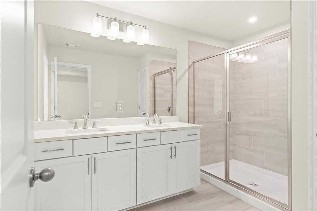 Modern master bathroom with double vanity, white cabinets, quartz counters, and frameless glass shower in Davidson Homes The Cary A, Kennesaw, GA