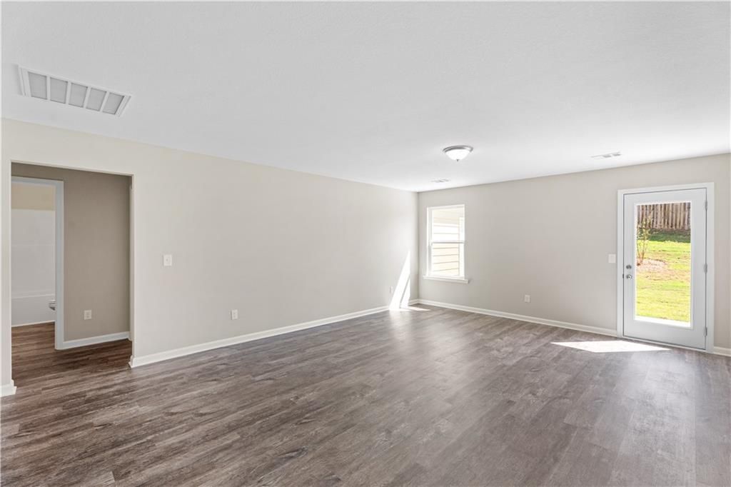 Spacious empty living room with beige walls, luxury vinyl plank flooring, and sliding door to grassy backyard in Davidson Homes The Washington, Phenix City