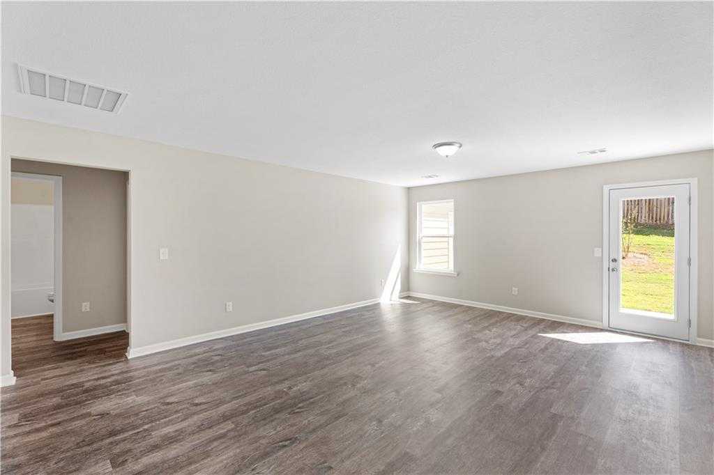 Spacious empty living room with beige walls, luxury vinyl plank flooring, and sliding door to grassy backyard in Davidson Homes The Washington, Phenix City