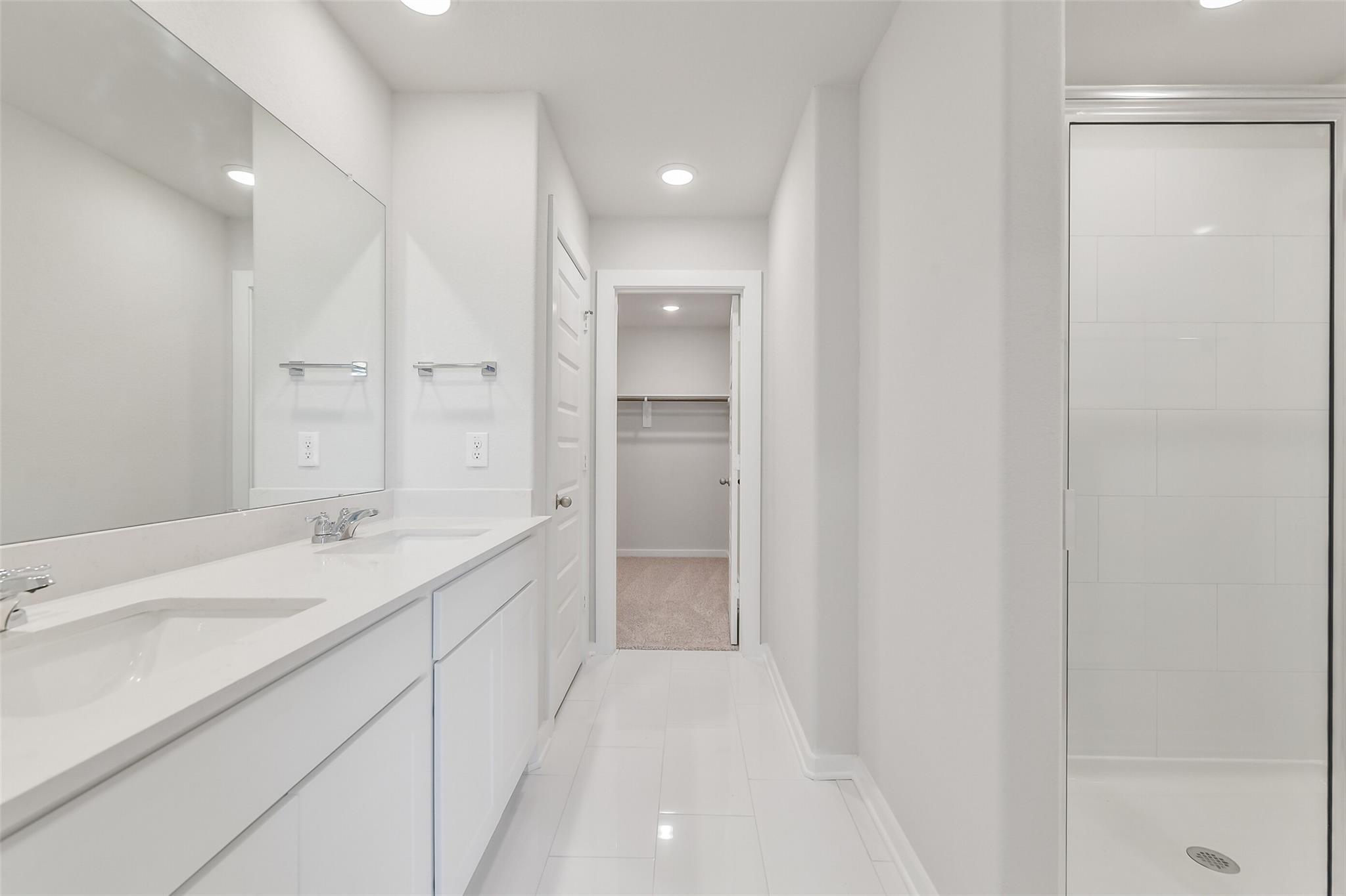 Modern master bathroom featuring double white vanity, frameless shower, and walk-in closet in Davidson Homes The Trinity F, Magnolia TX
