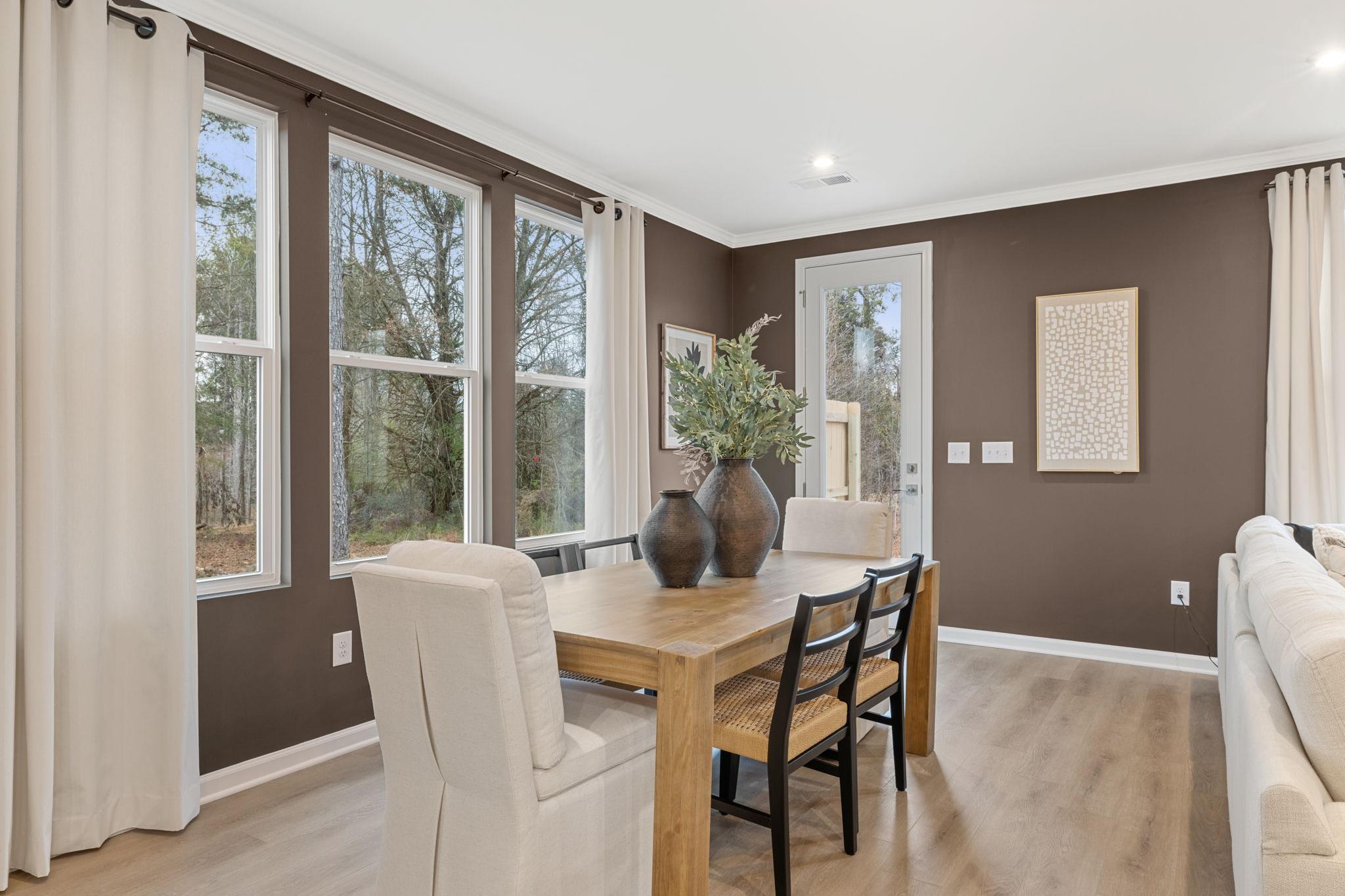 Spacious dining room at Lake Shore Winder GA featuring wooden table, large windows with tree views, and neutral decor by Davidson Homes