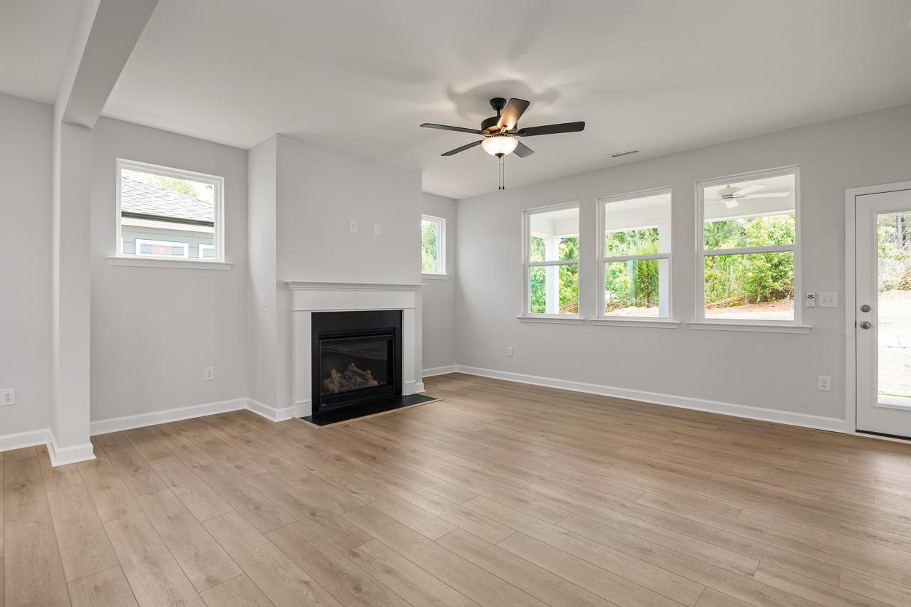 Spacious living room in The Birch II featuring a cozy fireplace, luxury vinyl flooring, and large windows.