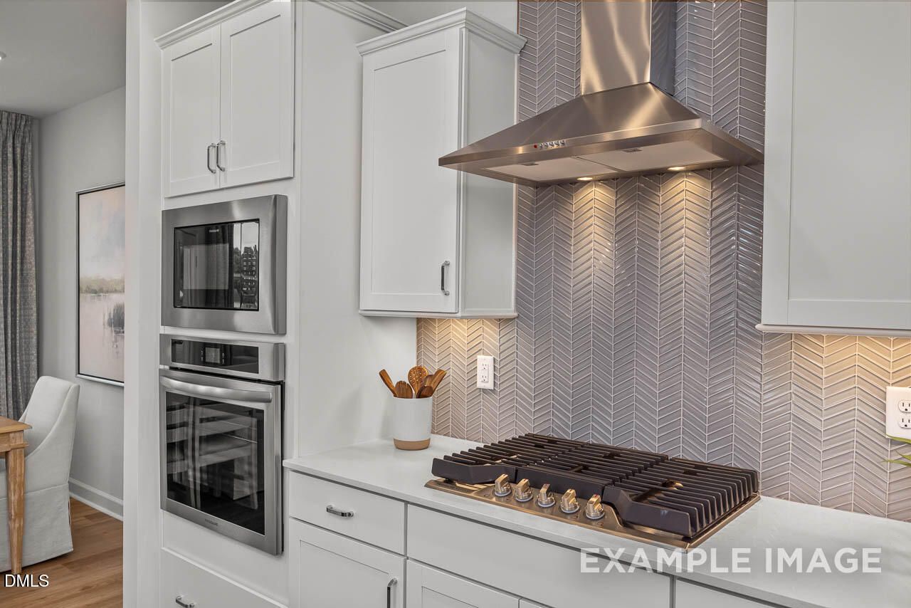 Modern kitchen with white shaker cabinets, stainless steel range and cooktop, herringbone backsplash in Davidson Homes The Graham, Fuquay-Varina NC