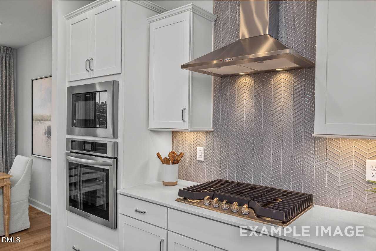 Modern kitchen with white cabinets, stainless steel gas range, herringbone backsplash in Davidson Homes The Graham, Fuquay-Varina, NC