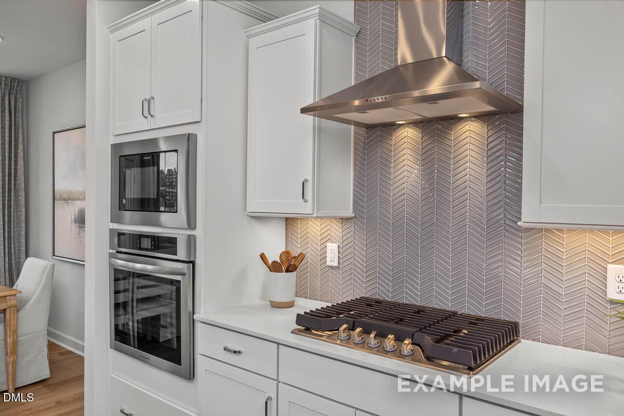 Modern kitchen featuring white cabinets, stainless steel range and hood, herringbone tile backsplash in Davidson Homes The Graham, Fuquay-Varina, NC