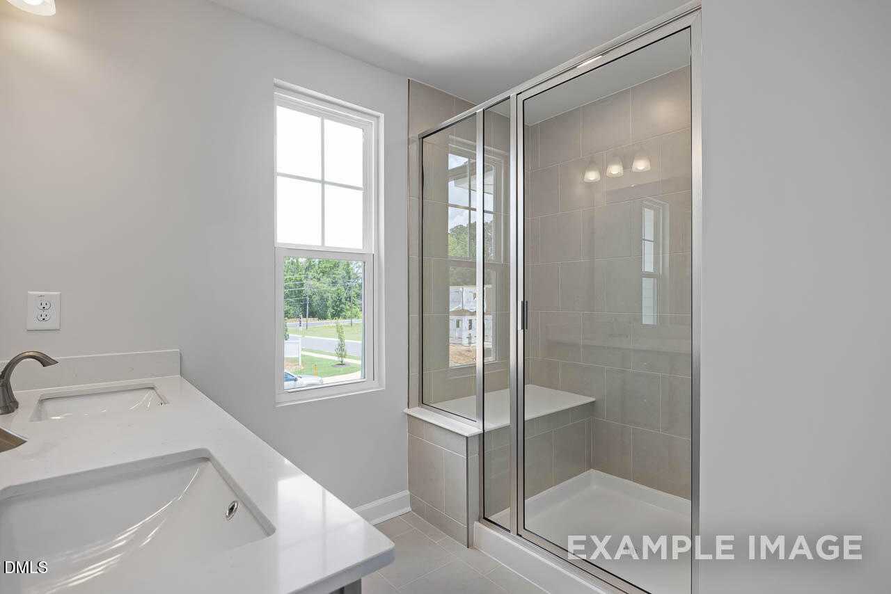 Modern master bathroom with double quartz vanity, frameless glass shower, and garden view in Davidson Homes The Warren, Fuquay-Varina, NC