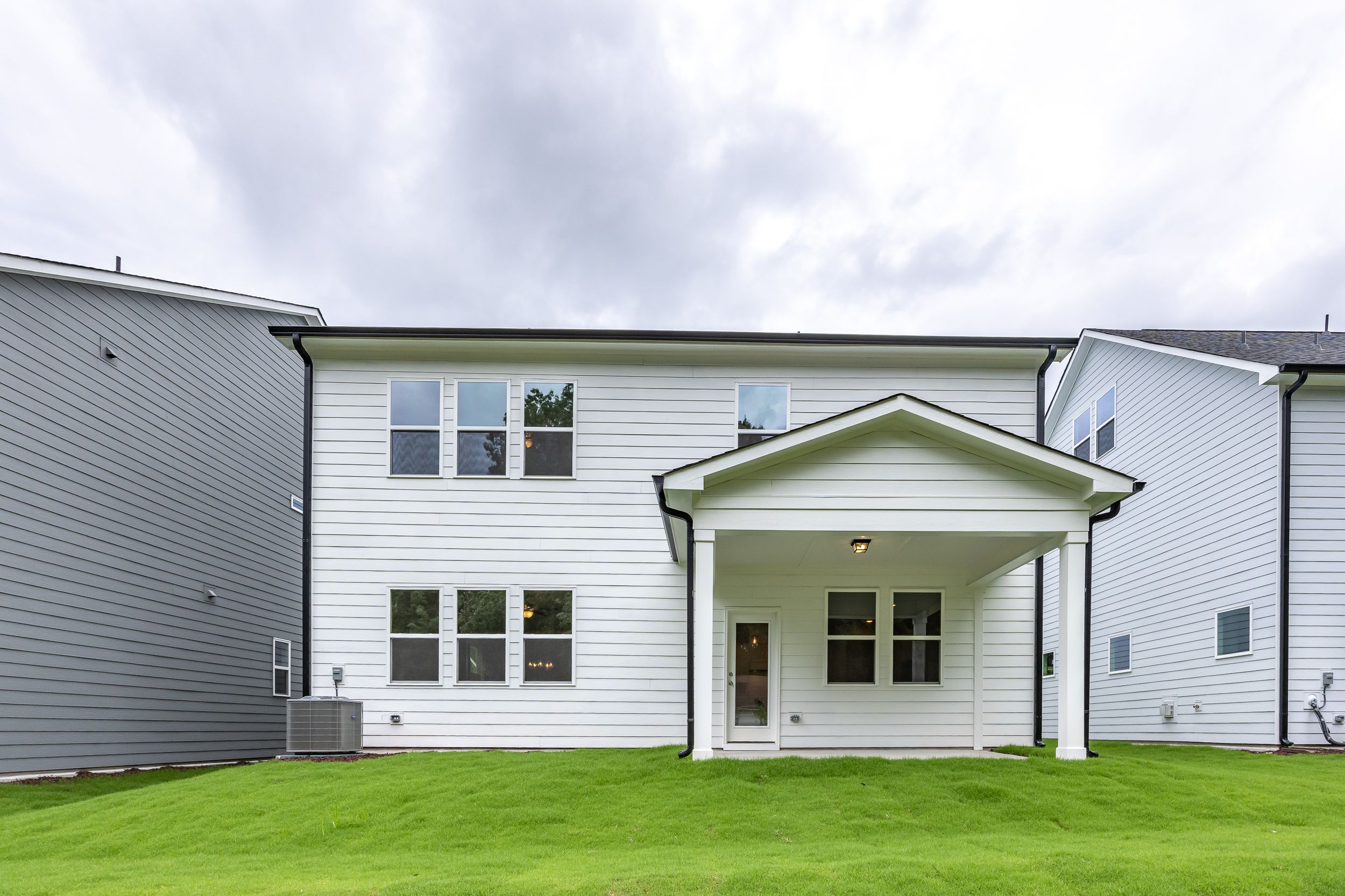 Rear elevation of The Beech A 2-story home by Davidson Homes, white siding, covered porch with columns, lush green backyard