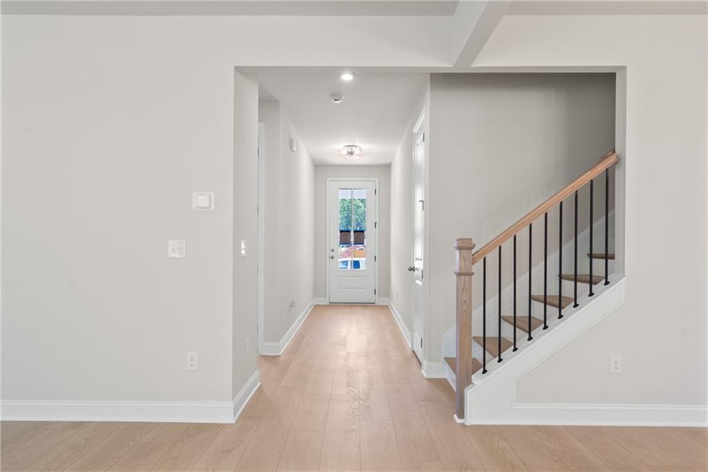 Elegant hallway with oak hardwood floors, wooden staircase, and glass French door in The Hickory E home, Buford, Georgia