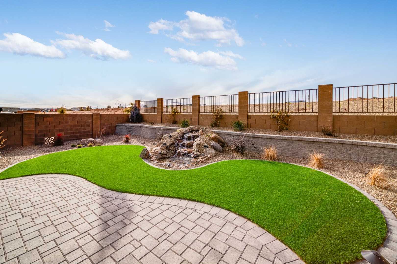 Spacious backyard patio in The Newport B Davidson Homes design with curved artificial turf, rock waterfall, paver stones, and desert landscaping in Prescott AZ