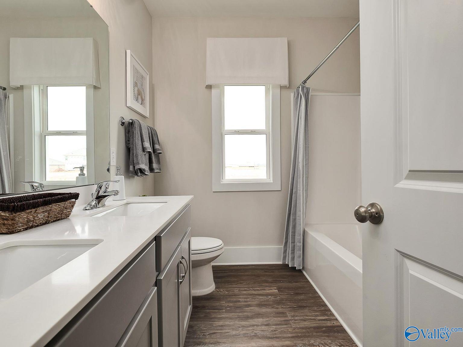 Modern guest bathroom featuring double vanity, gray cabinets, tub-shower combo, and hardwood floors in The Everett, Toney, AL
