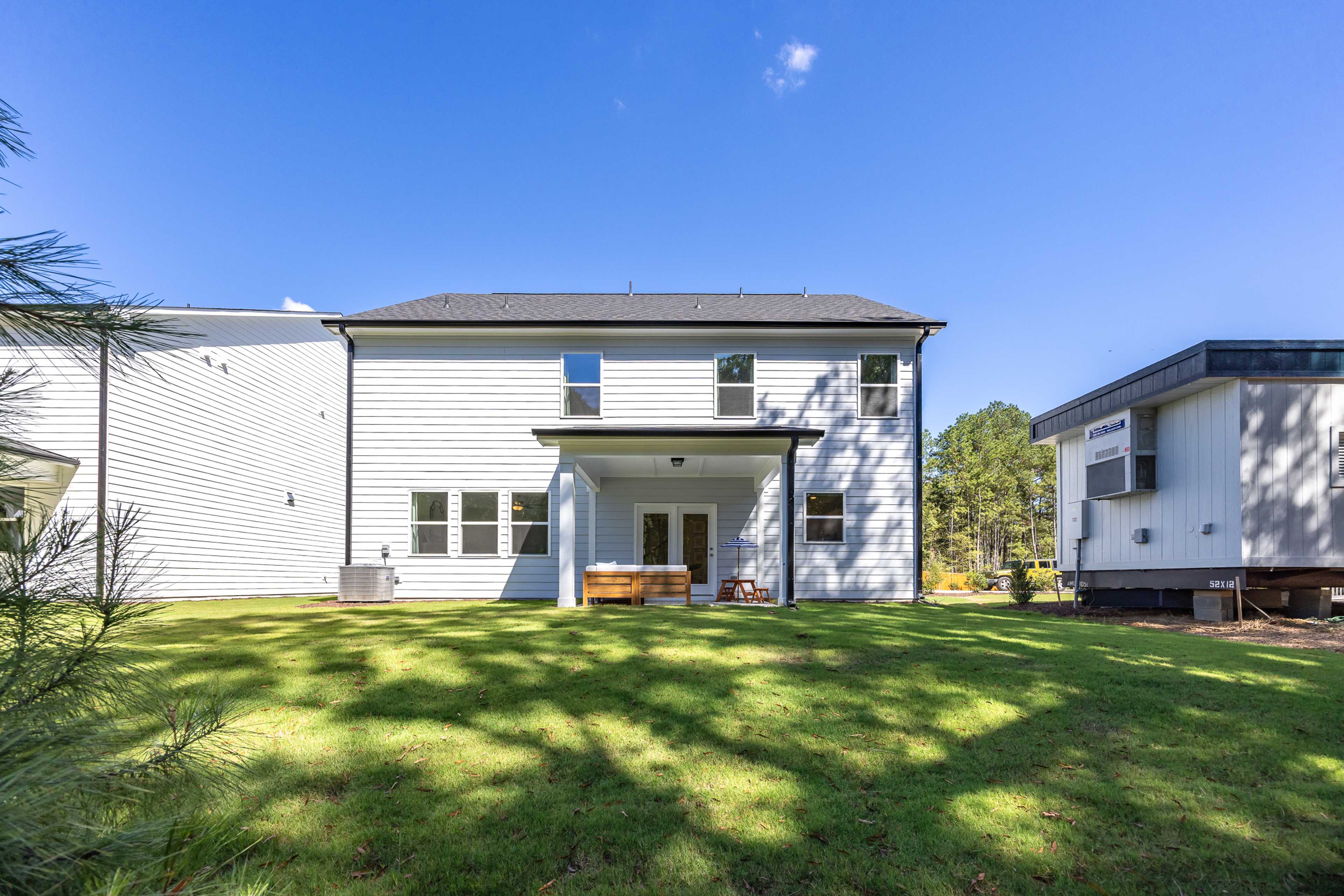 Modern two-story white home rear exterior at Sage on North Main in Wake Forest NC with covered deck, patio furniture, lush green lawn and pine trees