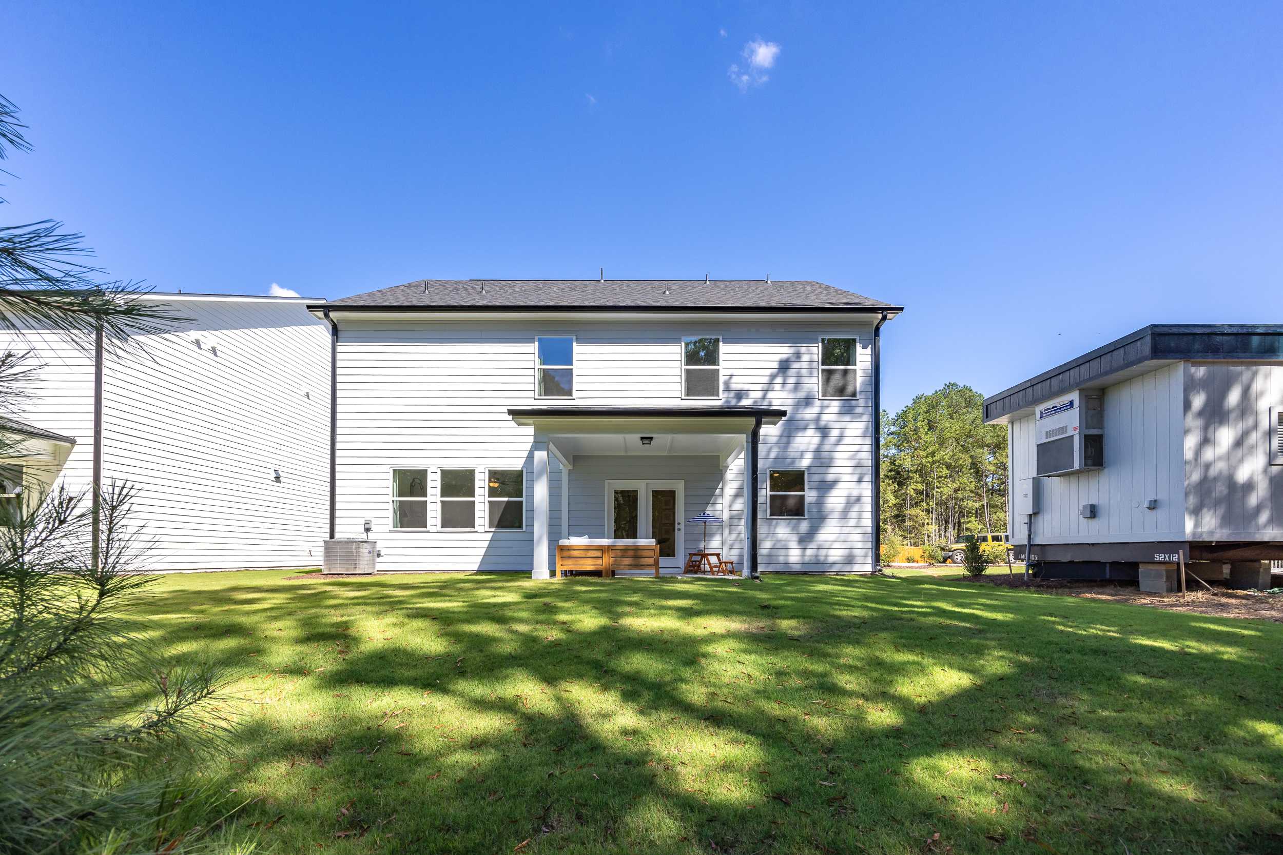 Modern two-story white home rear exterior at Sage on North Main in Wake Forest NC with covered deck, patio furniture, lush green lawn and pine trees