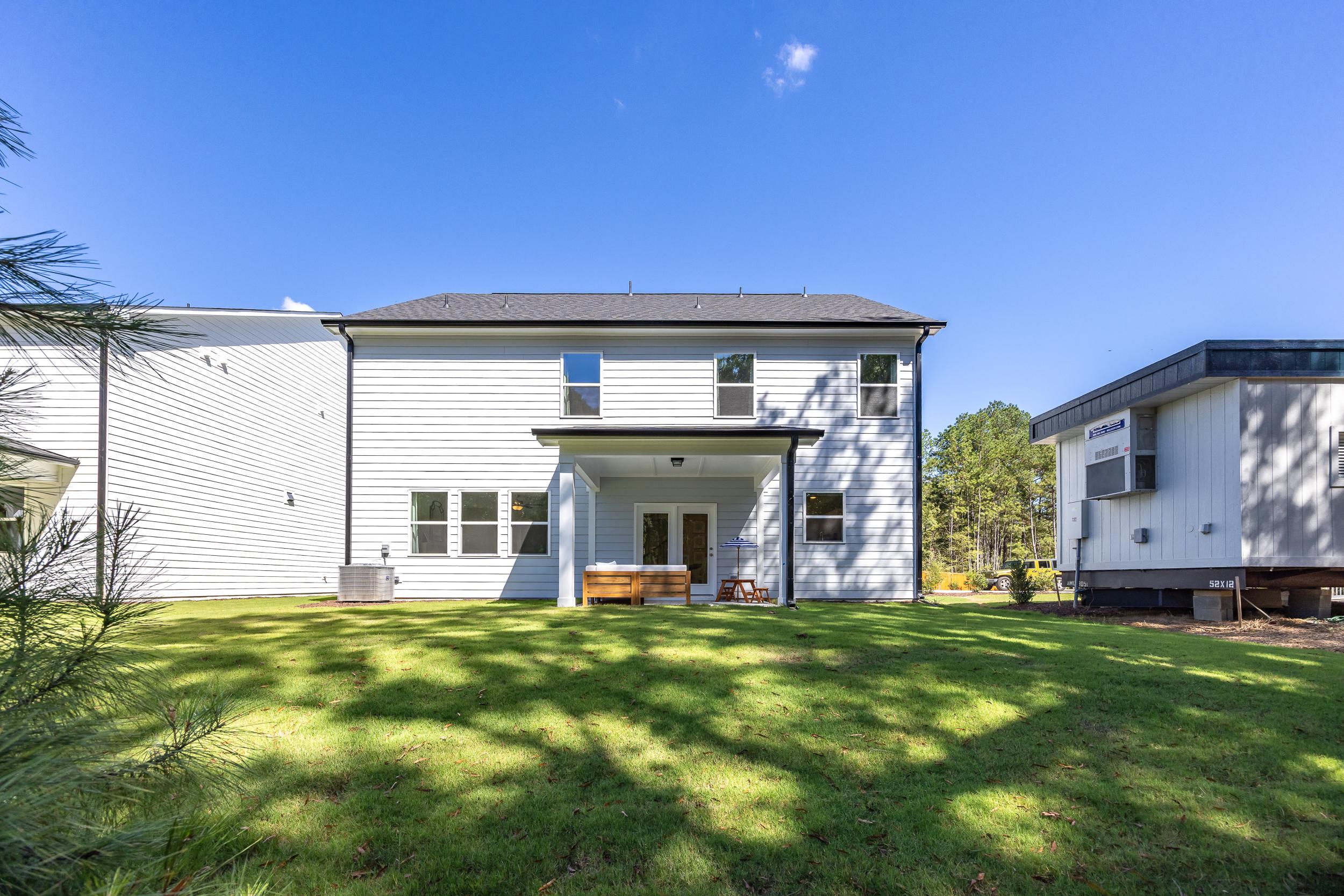 Modern two-story white home rear exterior at Sage on North Main in Wake Forest NC with covered deck, patio furniture, lush green lawn and pine trees
