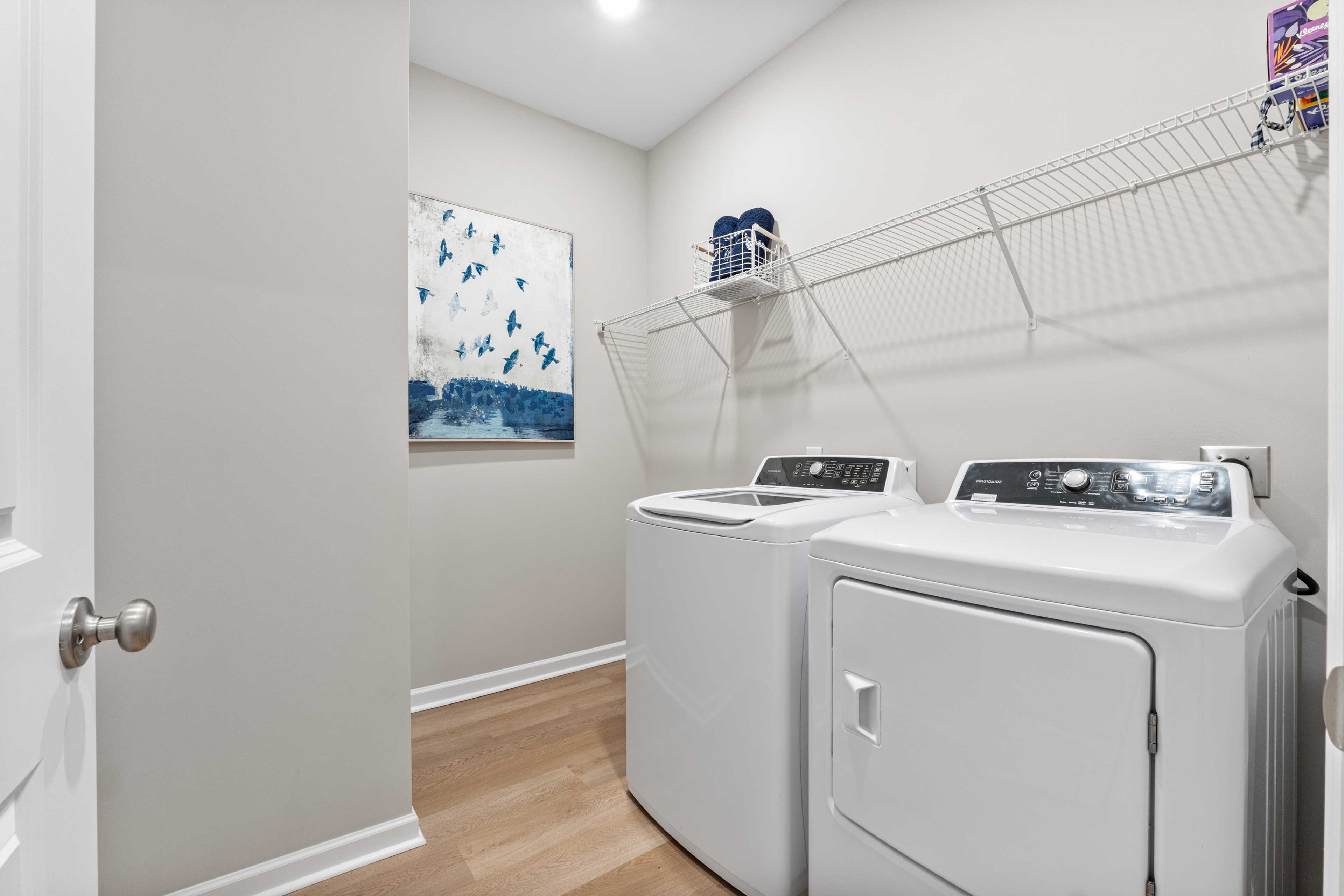 Spacious laundry room at Forest Glen in Hazel Green Alabama with white washer dryer hardwood floors blue wall art and wire shelving