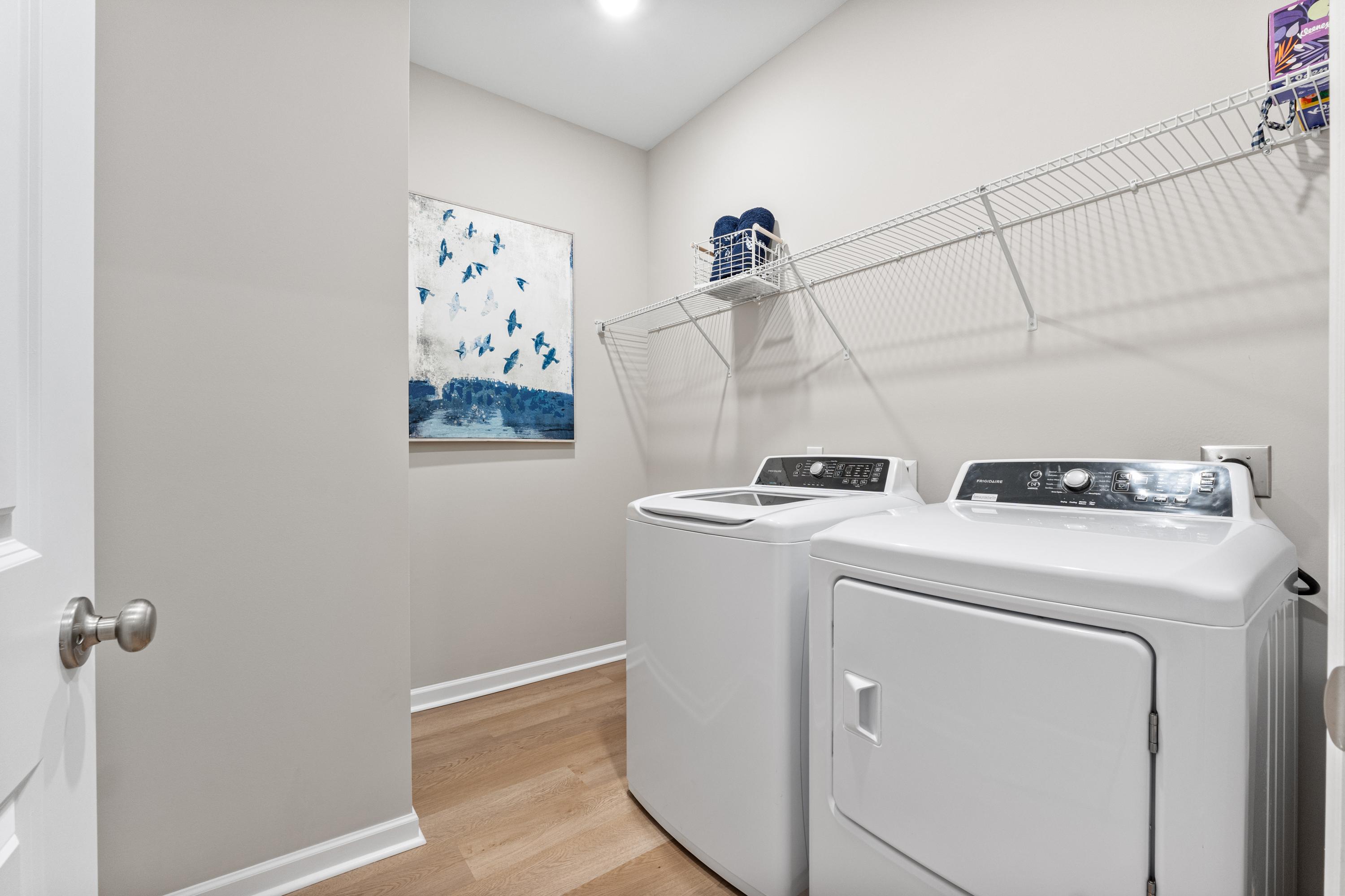 Spacious laundry room at Forest Glen in Hazel Green Alabama with white washer dryer hardwood floors blue wall art and wire shelving