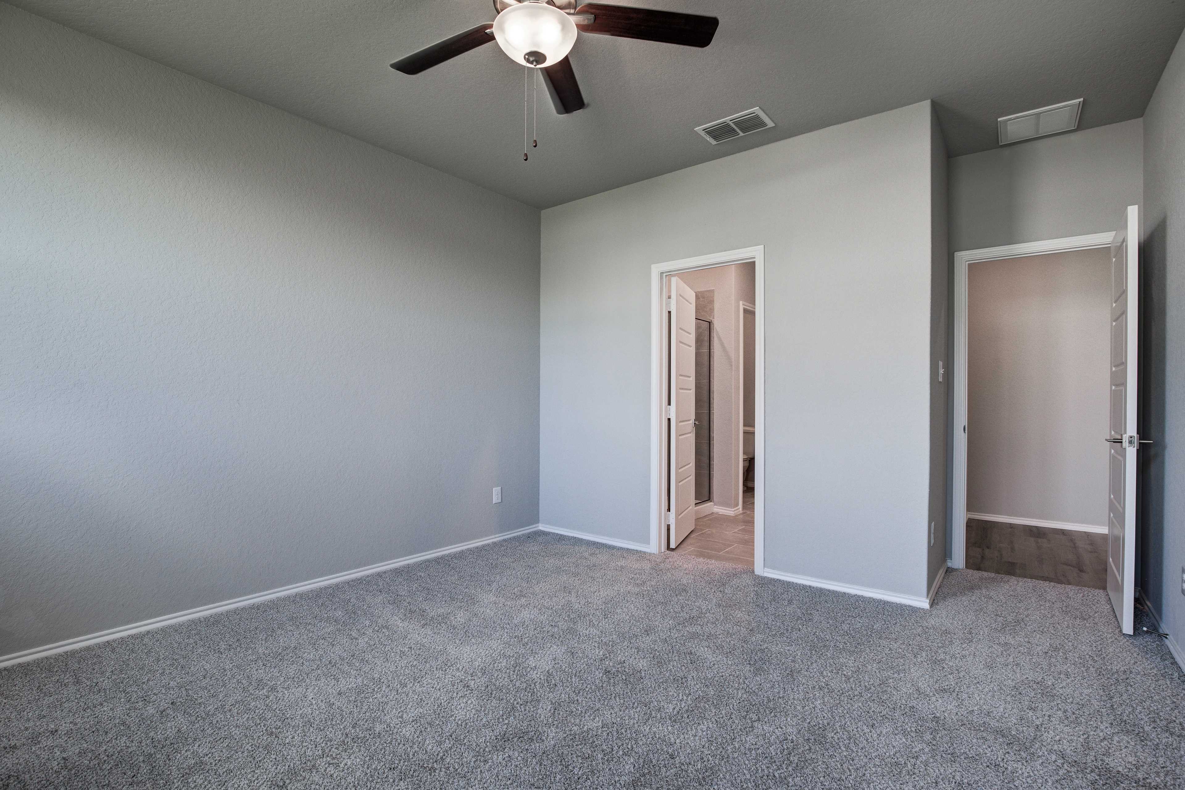 Spacious master bedroom in The Asheville with gray walls, carpet, ceiling fan, en-suite bath door, and closet access