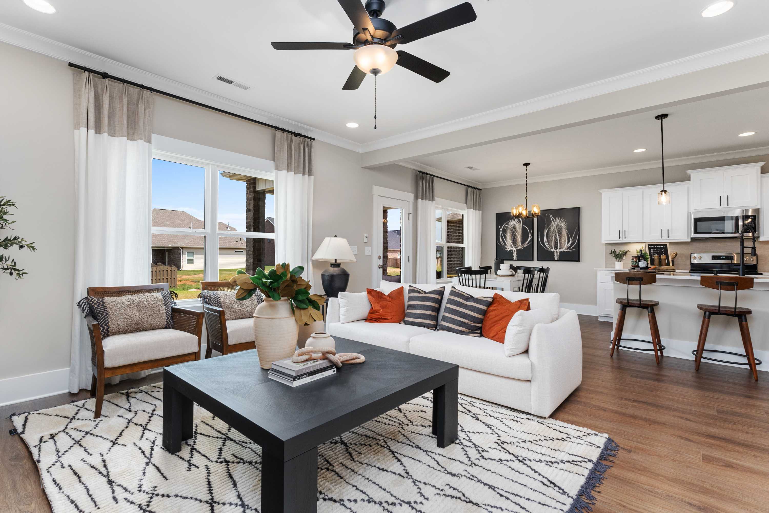 Cozy open-concept living room in The Shelby A with white sofa, orange accents, ceiling fan, and kitchen island view