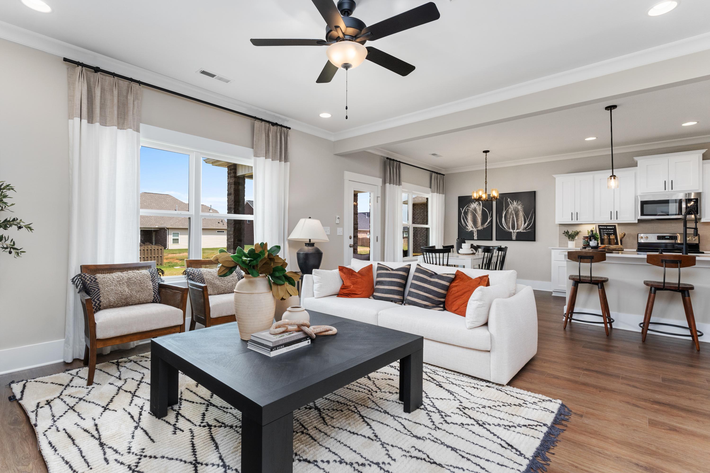 Cozy open-concept living room in The Shelby A with white sofa, orange accents, ceiling fan, and kitchen island view