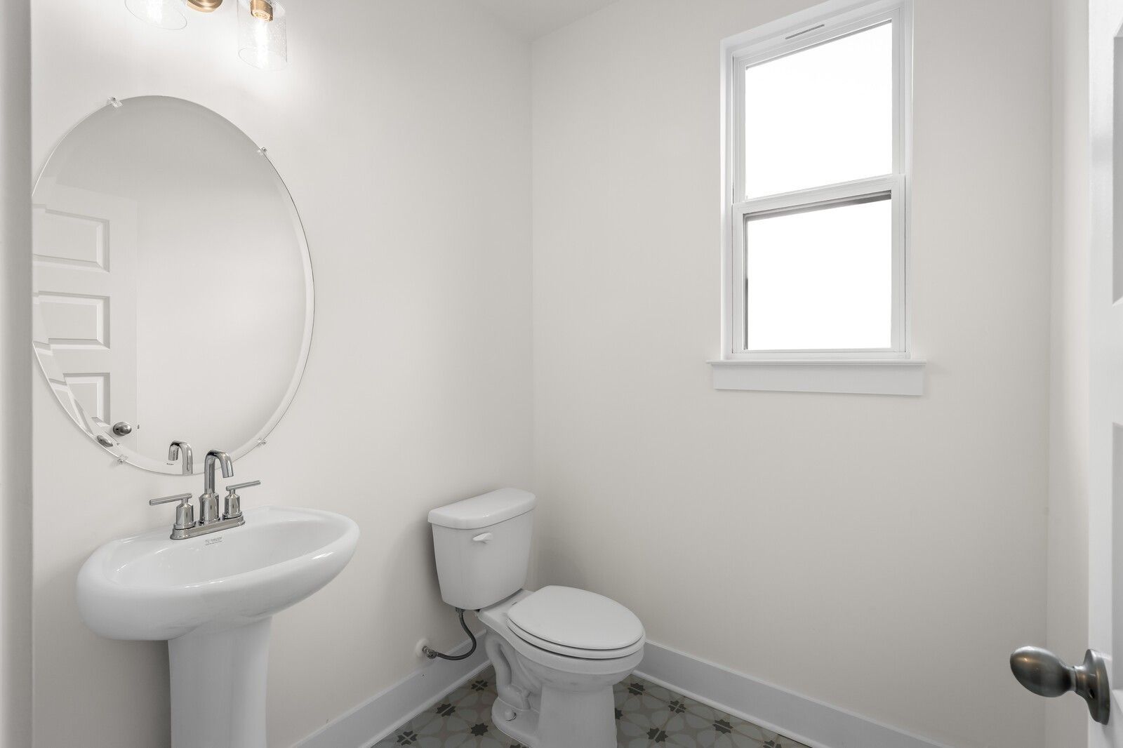 Modern powder room with pedestal sink, round mirror, and patterned tile floor in Davidson Homes The Henry C, Mt. Juliet.