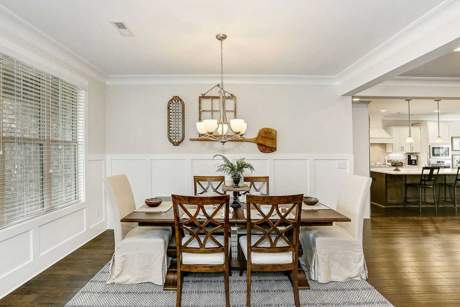 Spacious dining room in The Finleigh featuring wooden table, beige upholstered chairs, chandelier, and open kitchen view