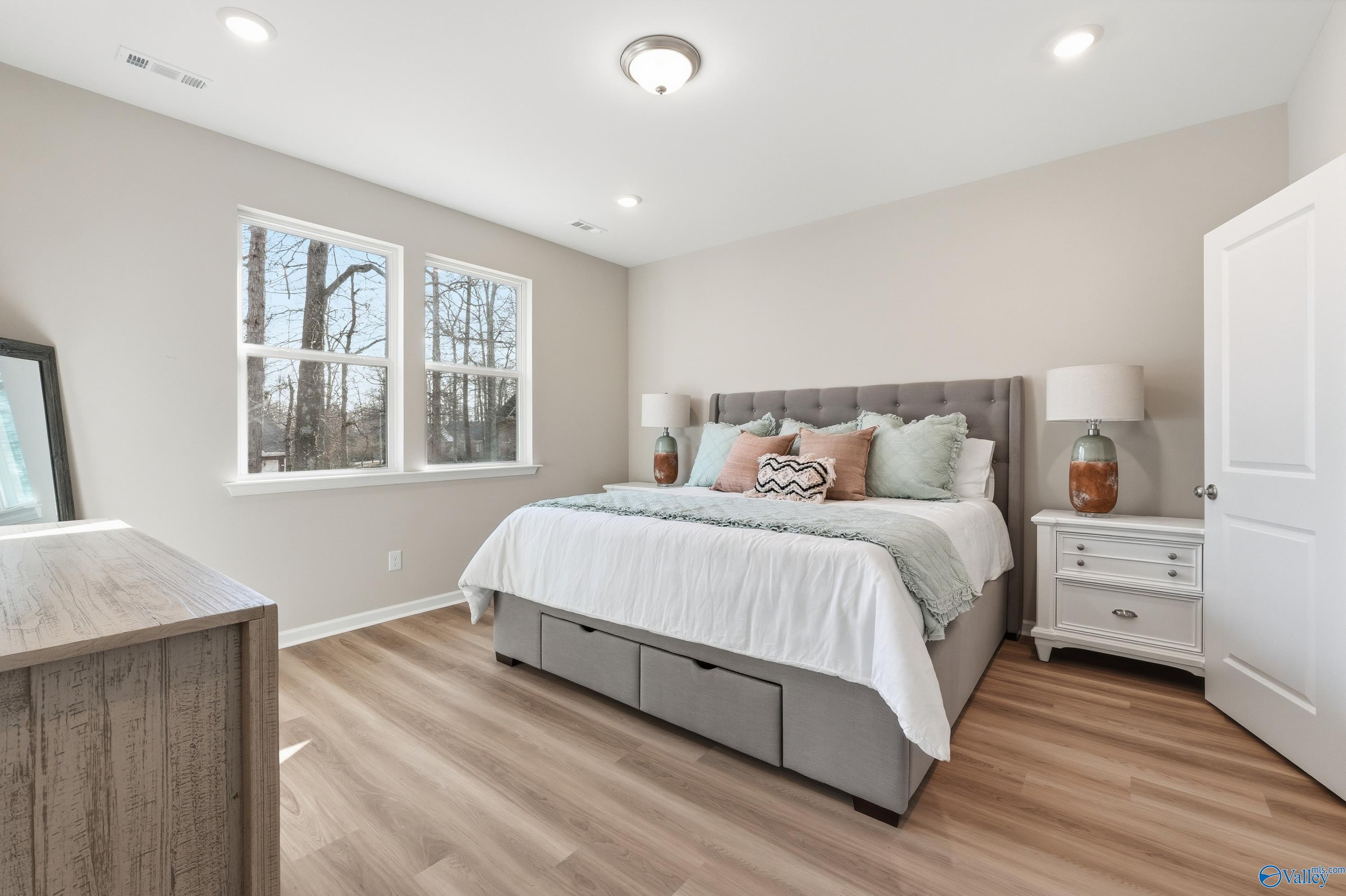 Serene master bedroom with king bed, gray headboard, teal pillows, large windows, and hardwood floors in Davidson Homes The Polaris, Fayetteville, TN