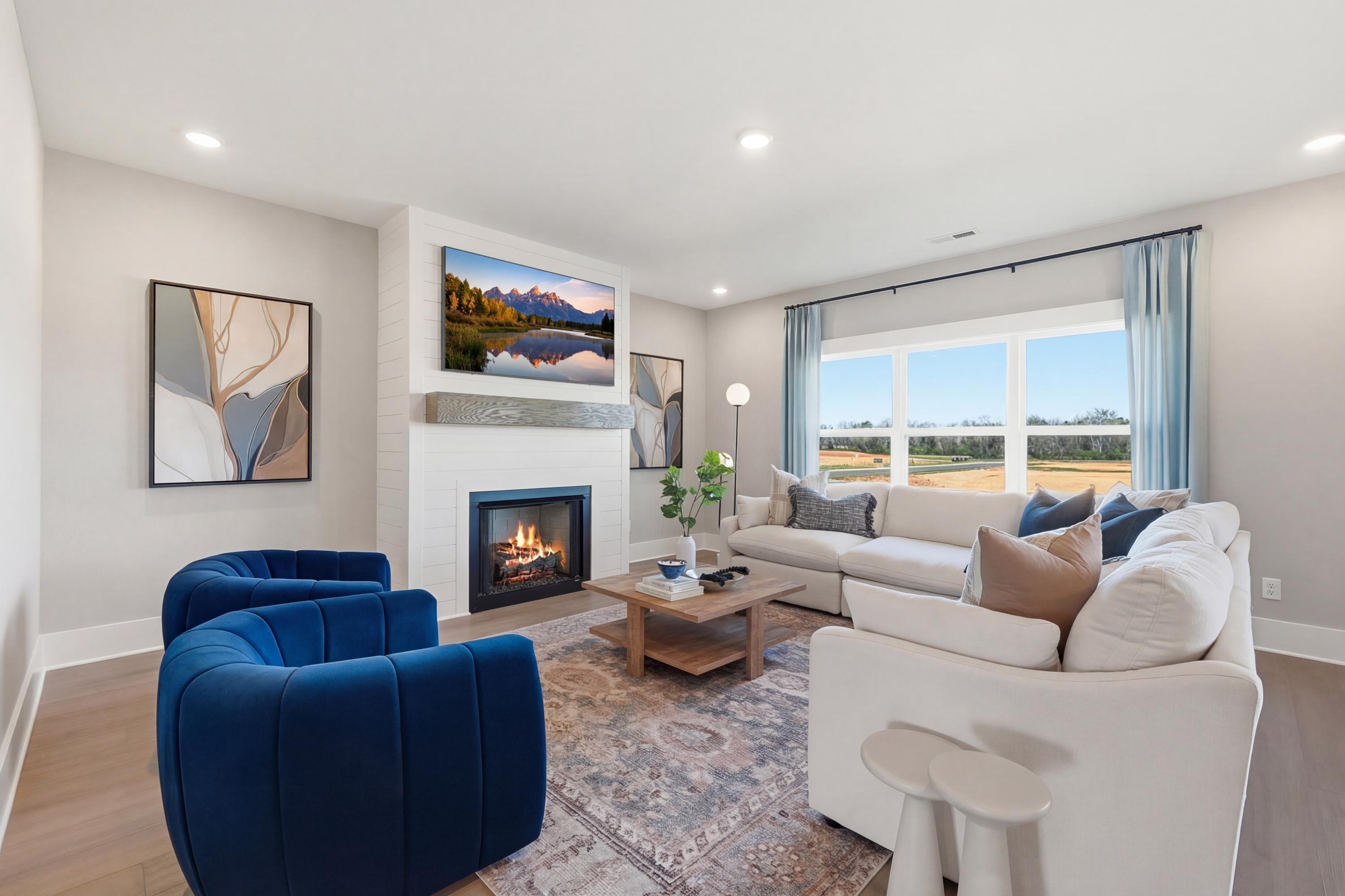 Cozy living room at Berry Cove in New Market Alabama with white sectional sofa, blue accent chairs, stone gas fireplace, mounted TV, and large windows