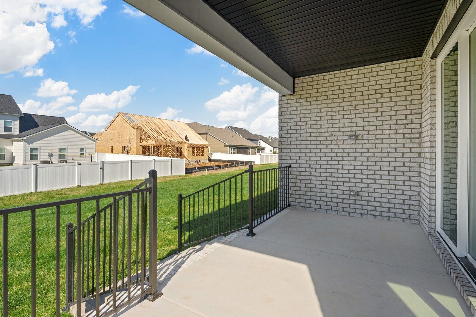 Covered back patio with white brick exterior, black metal railing, and lush green yard in Shelton Square, Murfreesboro, TN Hawkins floor plan by Davidson Homes