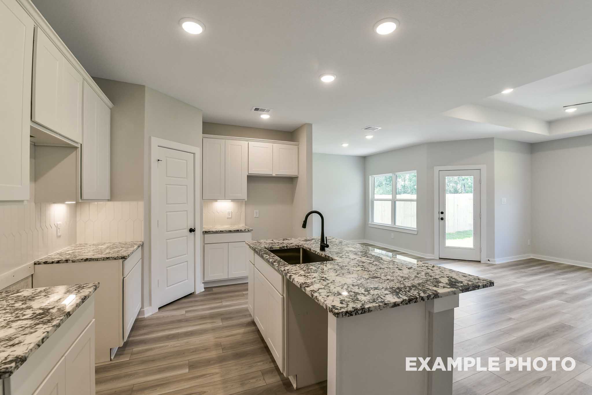 Spacious modern kitchen in The Daphne G featuring white cabinets, granite island, black faucet, and open layout
