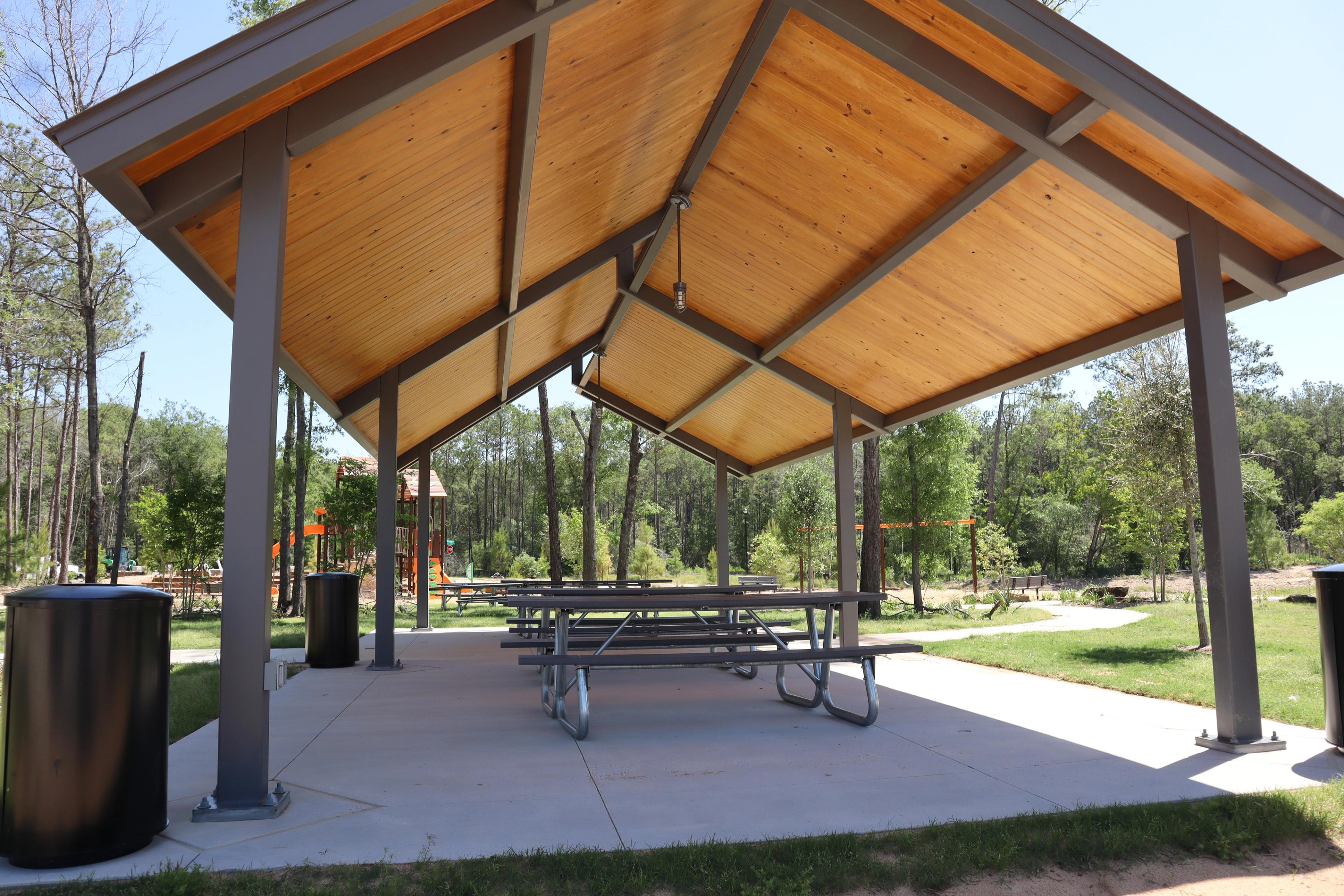 Spacious wooden pavilion with picnic tables at Robins Landing in Houston Texas, surrounded by trees and playground