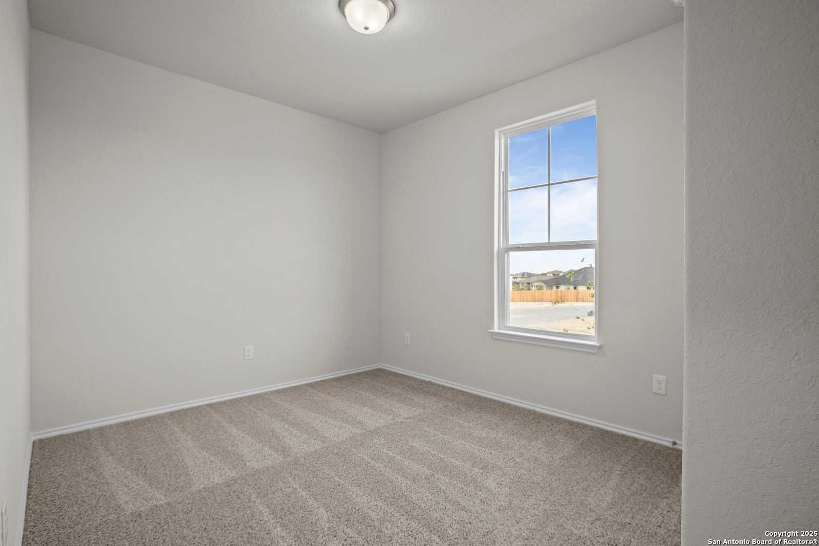 Bright empty secondary bedroom with neutral walls, beige carpet, and large window in Davidson Homes The Asheville J, San Antonio, Texas