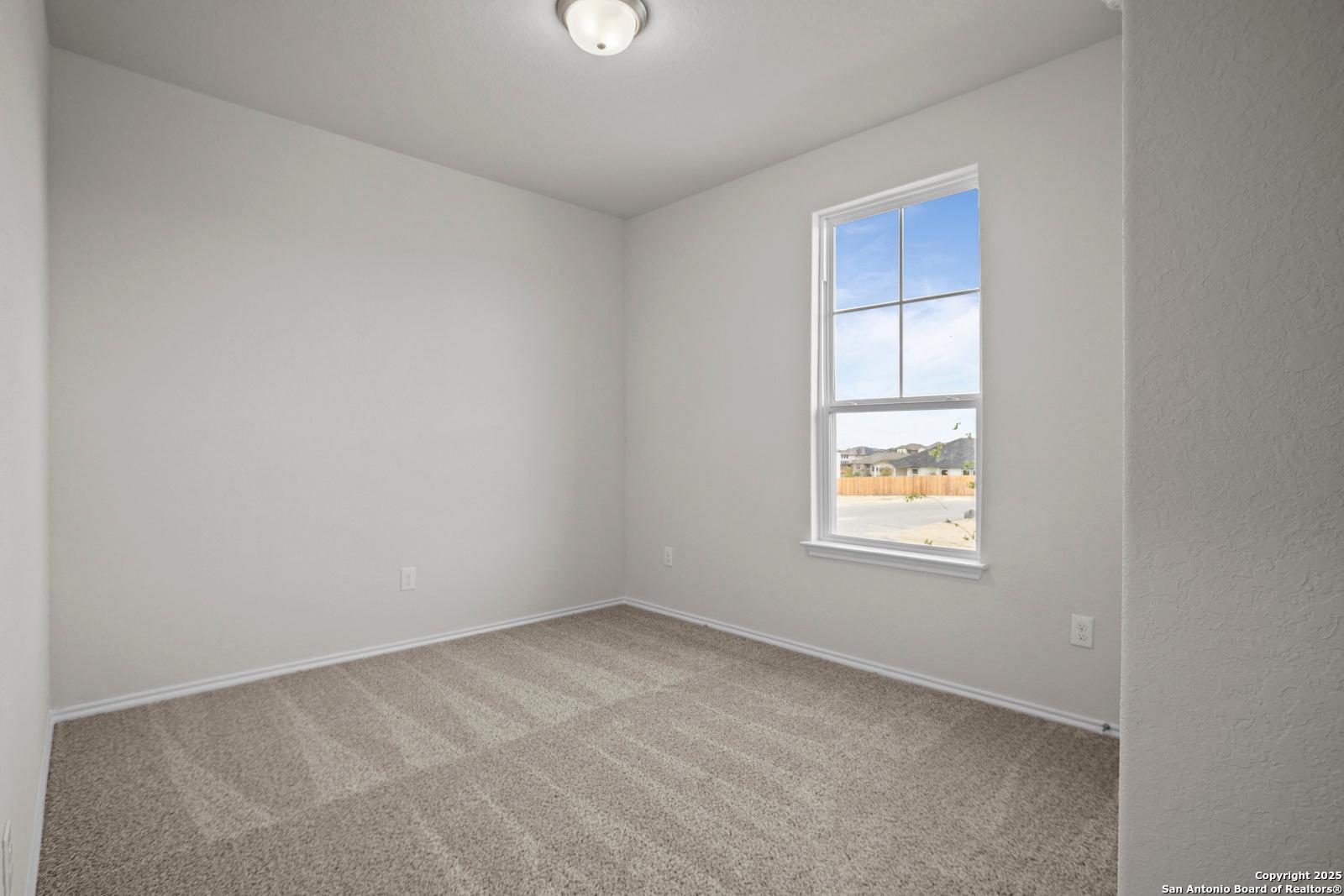 Bright empty secondary bedroom with neutral walls, beige carpet, and large window in Davidson Homes The Asheville J, San Antonio, Texas