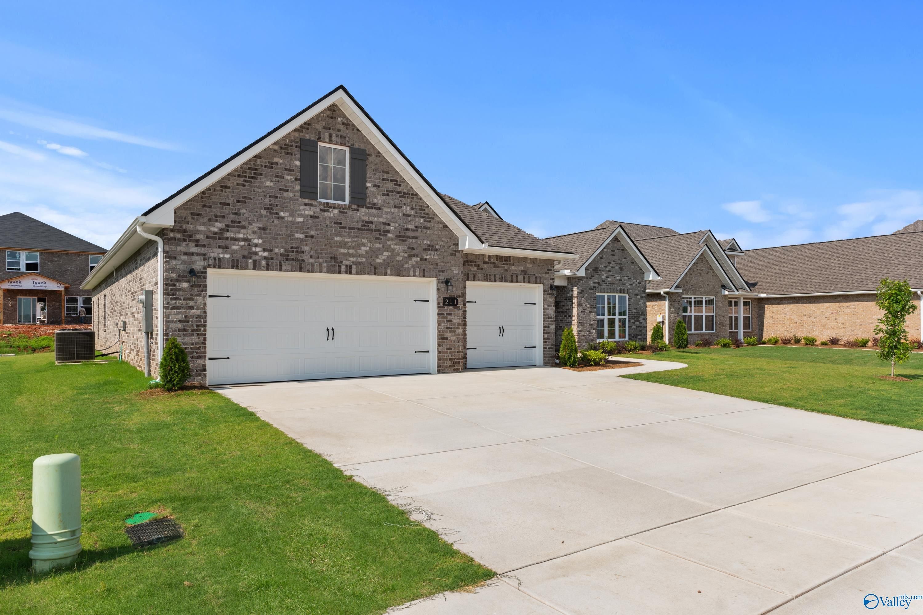 Modern gray brick single-story home with 3-car garage, driveway, and lush green lawn in Kendall Farms, Toney, Alabama by Davidson Homes The Finleigh