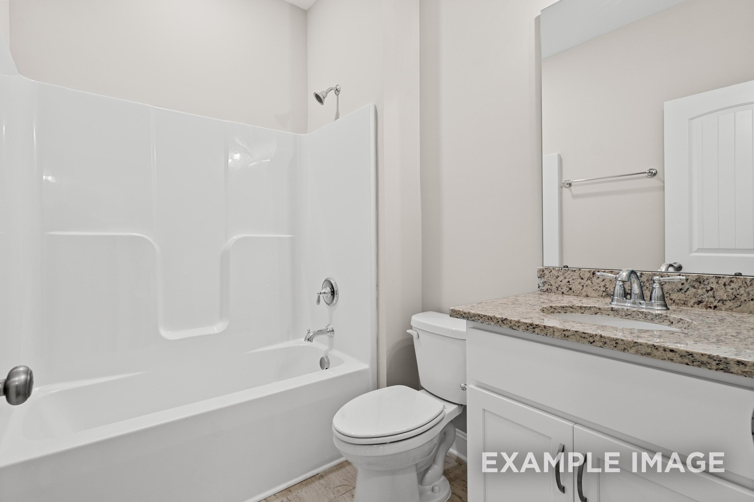 Spacious master bathroom in The Madison B featuring white tub, glass shower, granite vanity, toilet, and large mirror