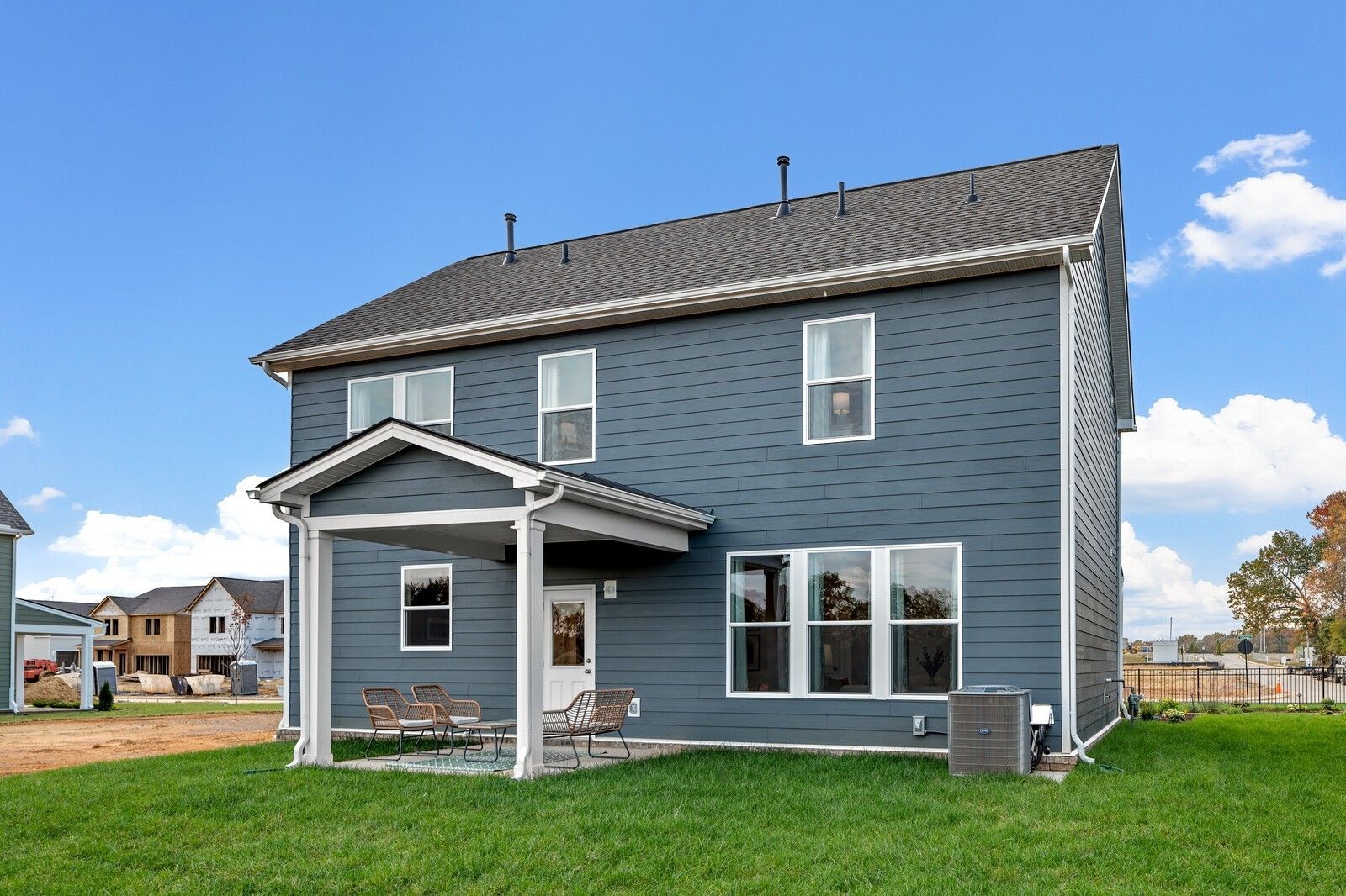 Two-story blue-sided home with covered back patio, wicker seating, large windows, and green yard in Sage Farms, White House, TN