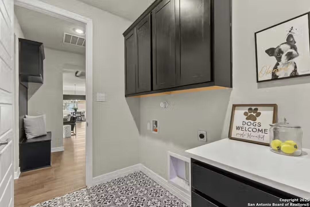 Modern laundry room featuring dark cabinets, white countertop, pet door, and dog-themed decor in Davidson Homes The Summerlin B, Castroville, TX