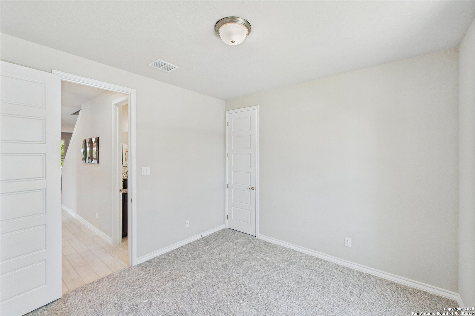 Cozy secondary bedroom featuring neutral beige walls, gray carpet, ceiling fan light, and framed art in Davidson Homes The Jennings H, Ladera, San Antonio