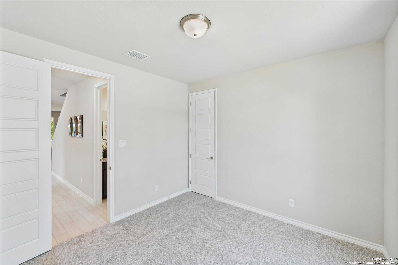 Cozy secondary bedroom featuring neutral beige walls, gray carpet, ceiling fan light, and framed art in Davidson Homes The Jennings H, Ladera, San Antonio