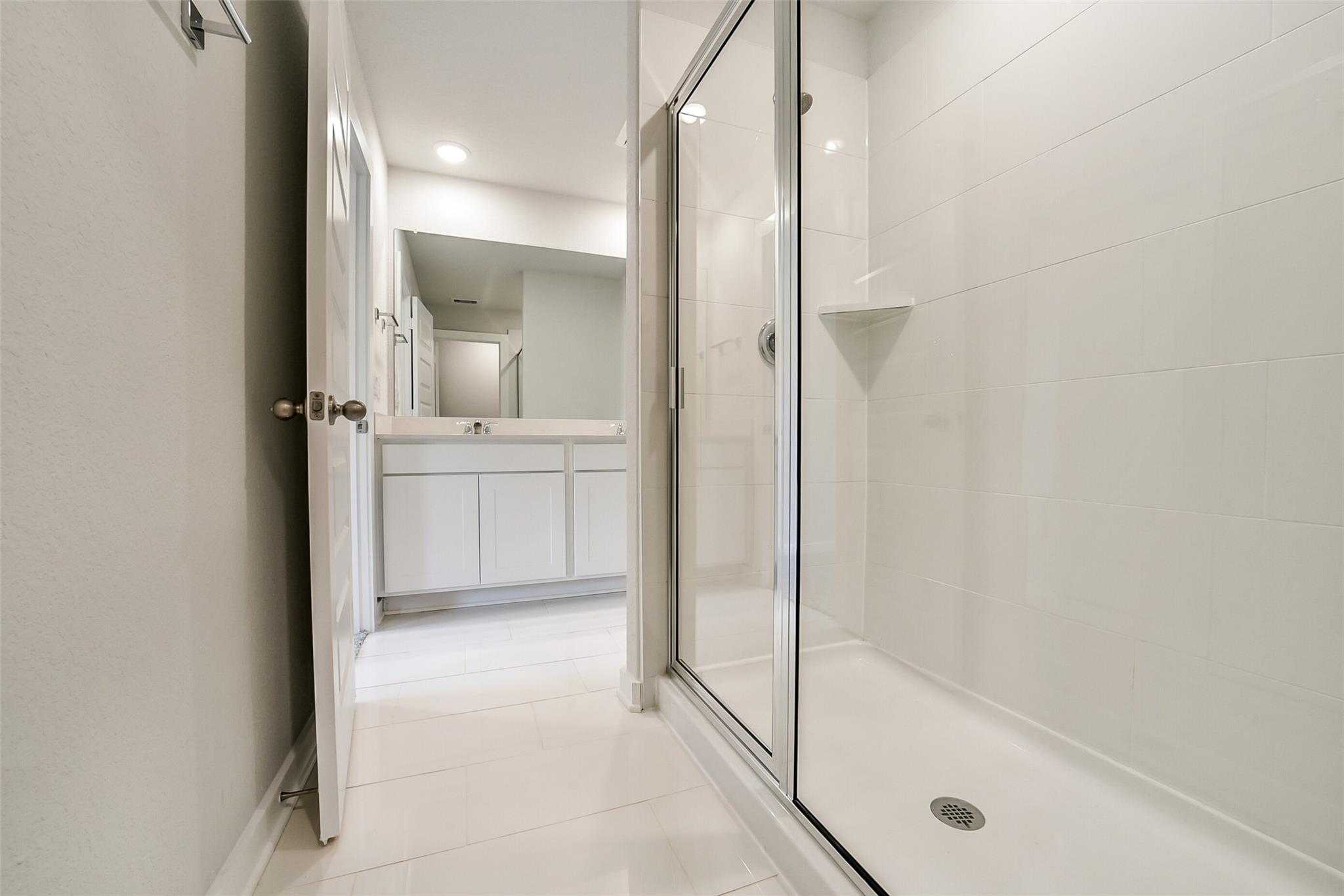 Modern master bathroom featuring frameless glass shower, double vanity, and white subway tiles in Davidson Homes The Trinity F, Magnolia, Texas