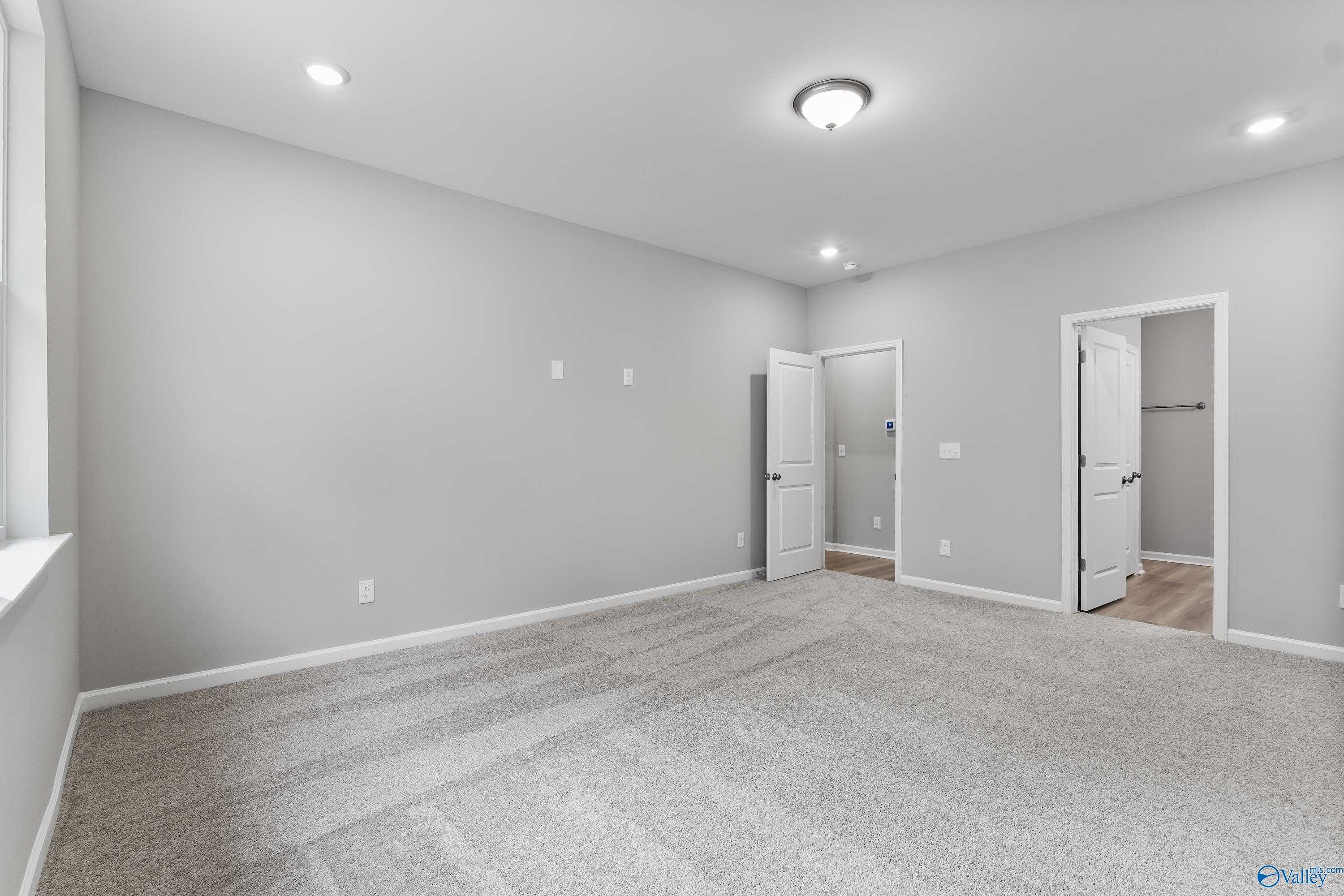 Empty secondary bedroom featuring gray walls, beige carpet, and attached bath door in Evermore Homes The Grace, Madison, Alabama