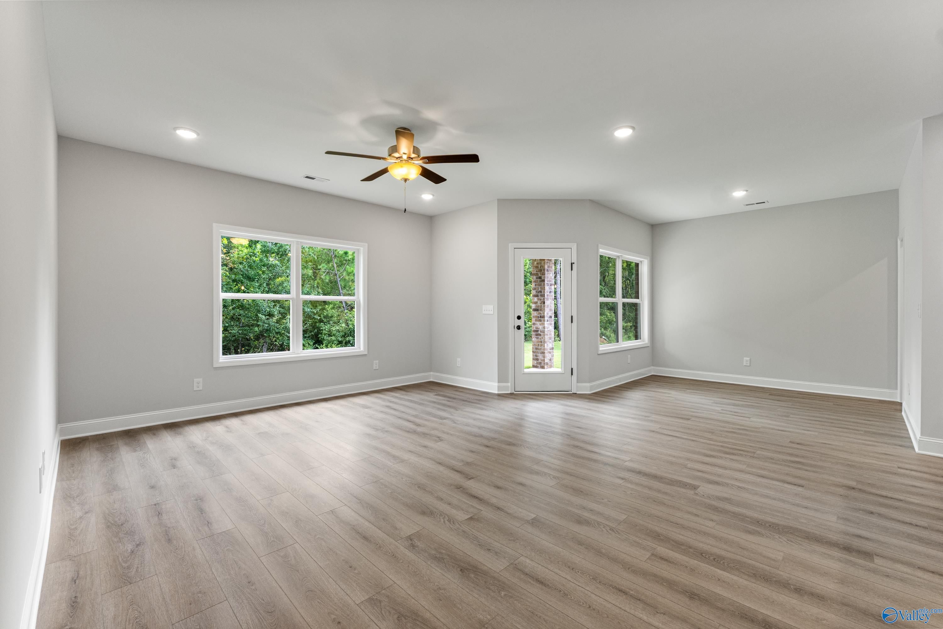 Spacious living room with light gray walls, hardwood floors, ceiling fan, and large green-view windows in Davidson Homes The Daphne, Huntsville AL