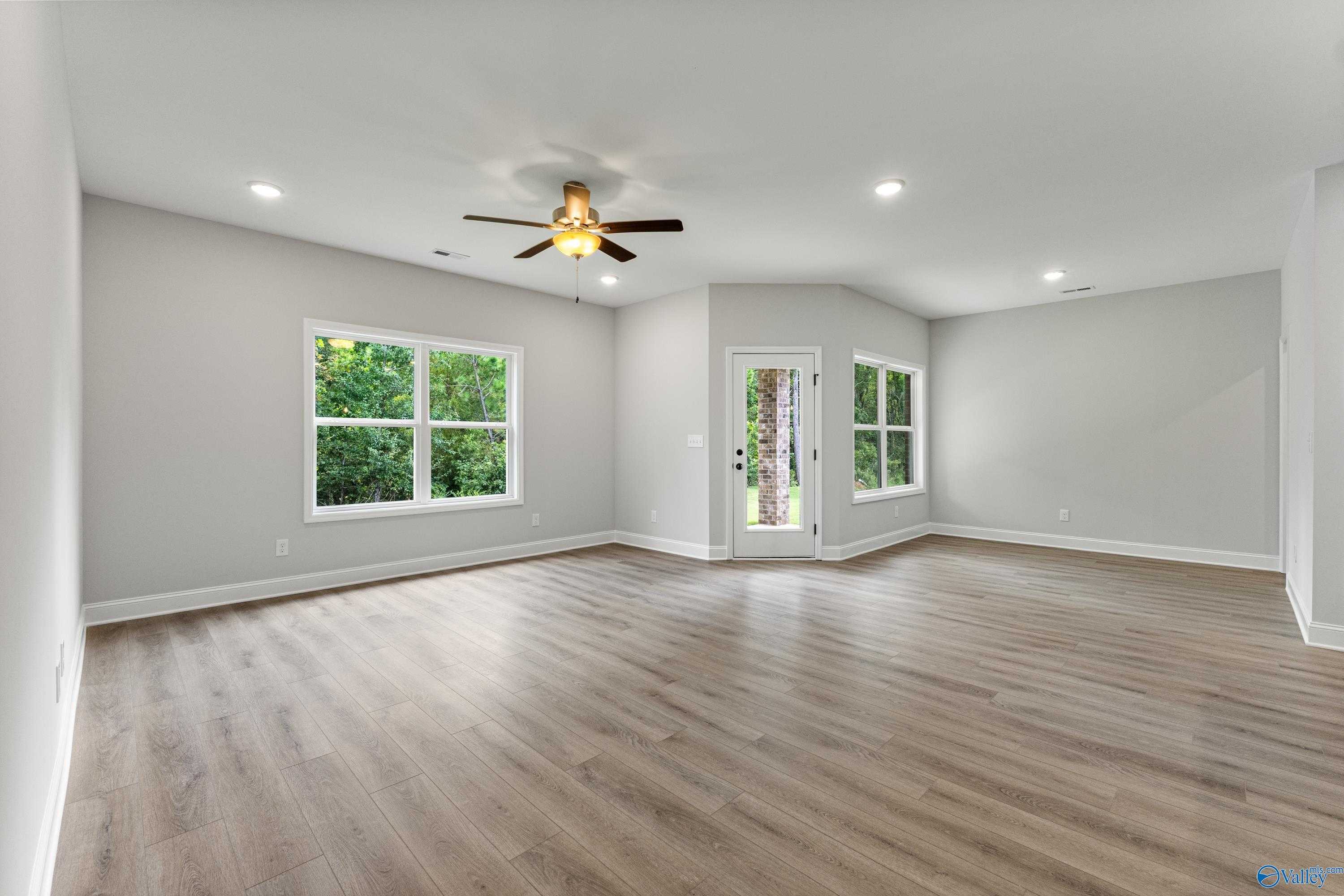 Spacious living room with light gray walls, hardwood floors, ceiling fan, and large green-view windows in Davidson Homes The Daphne, Huntsville AL
