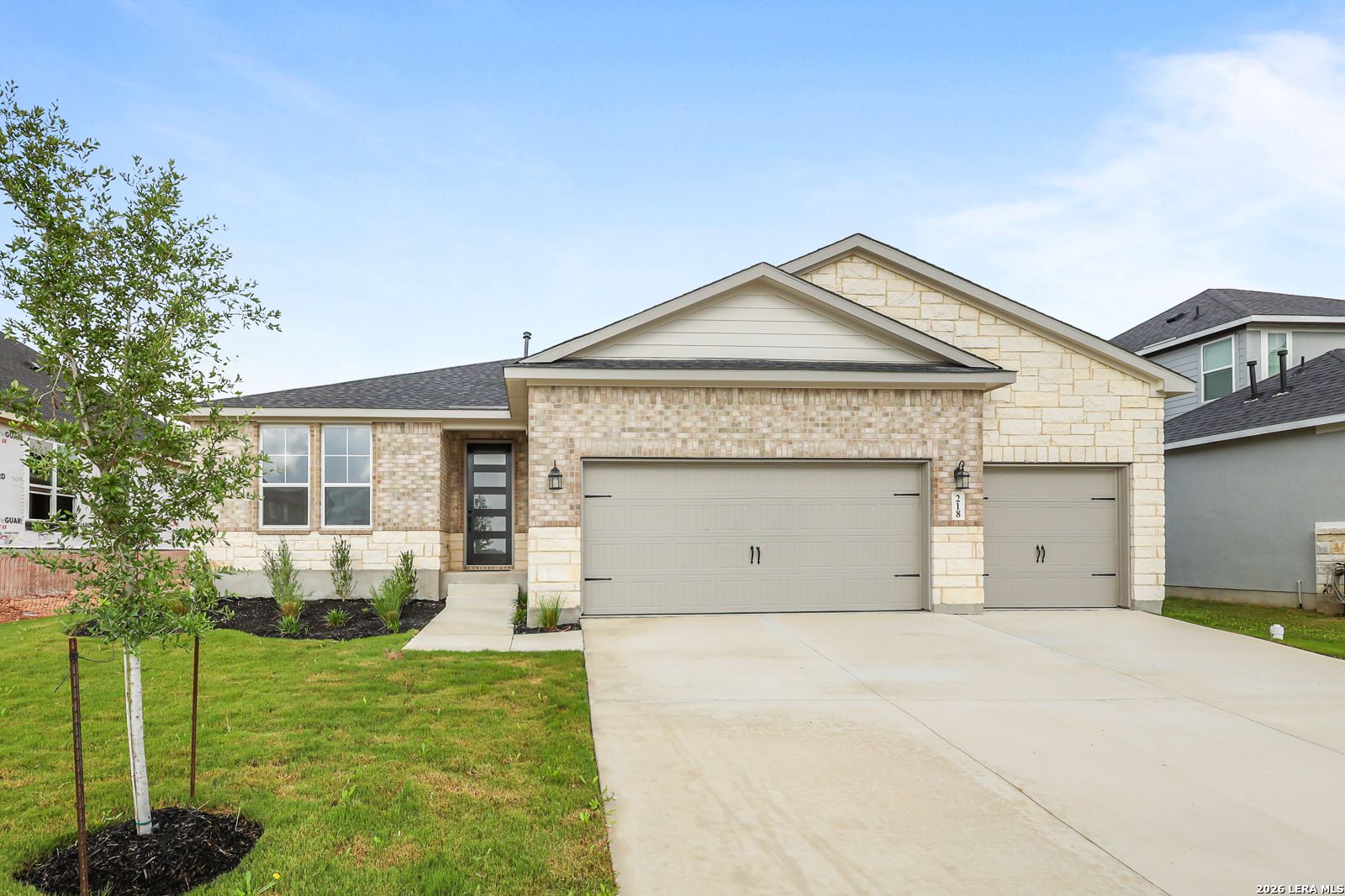 Modern 1-story brick and stone home with 2-car garage, front yard landscaping in The Reserve at Potranco Oaks, Castroville, Texas