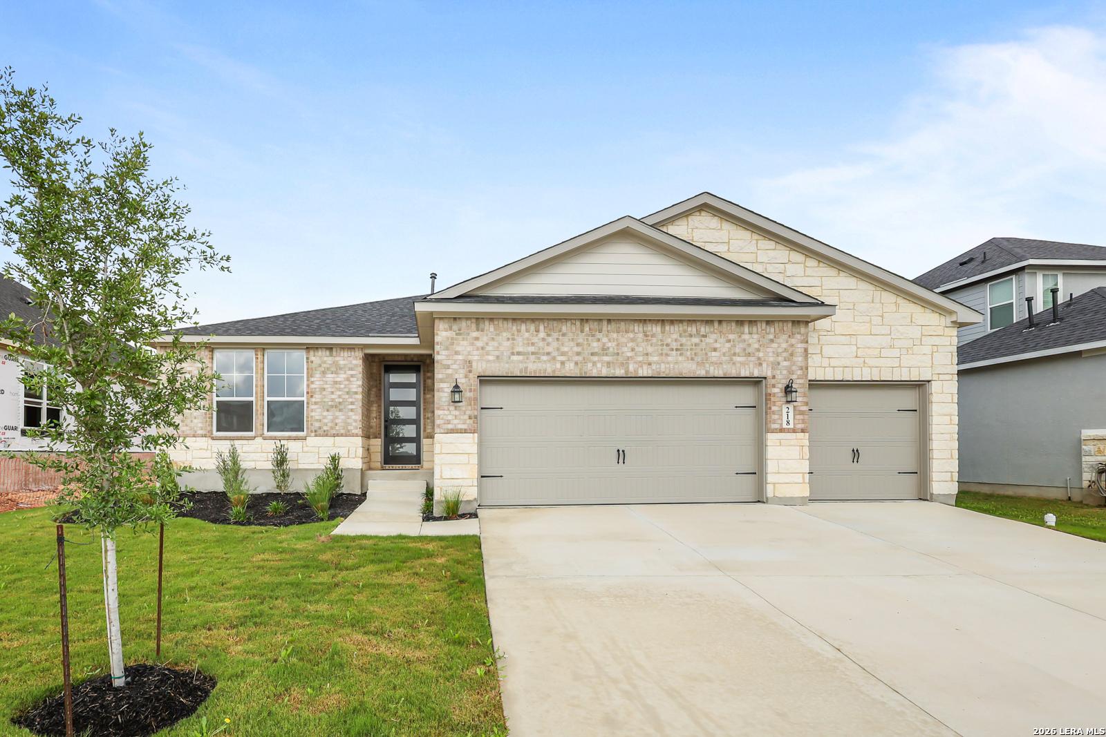 Modern 1-story brick and stone home with 2-car garage, front yard landscaping in The Reserve at Potranco Oaks, Castroville, Texas