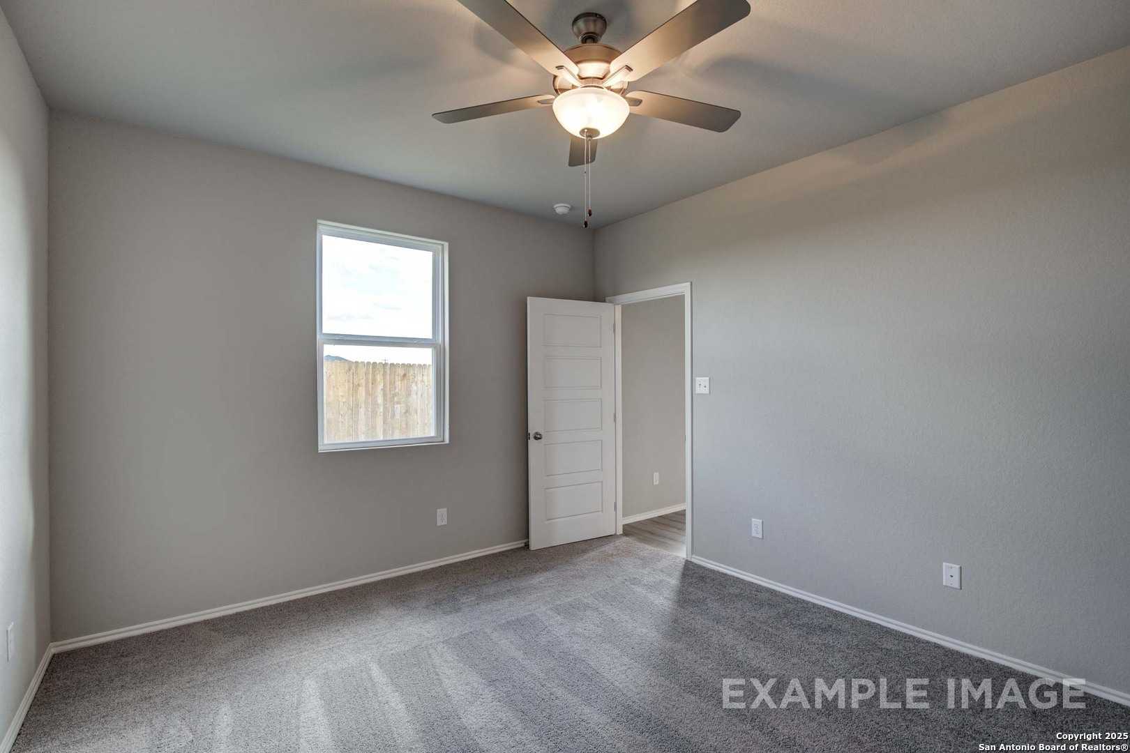 Spacious secondary bedroom with gray walls, ceiling fan, and window overlooking backyard in Davidson Homes The Blanco C, San Antonio