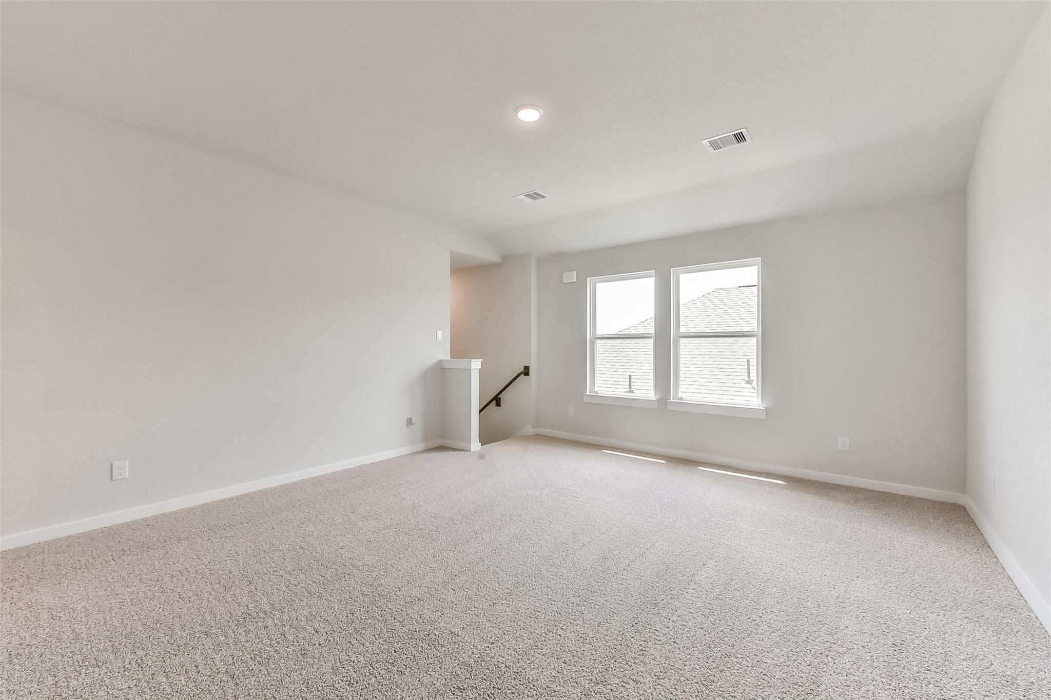 Spacious upstairs loft with beige carpet, large windows, and staircase in Davidson Homes The Tierra C, Dayton, Texas