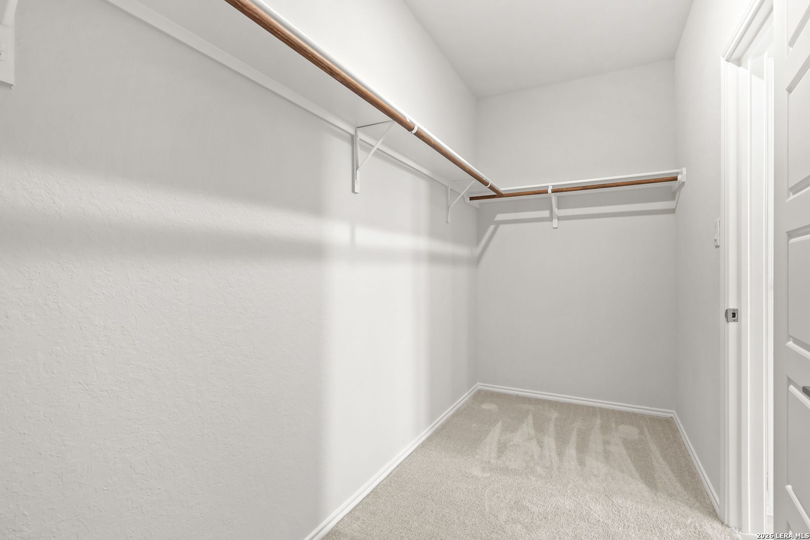 Spacious walk-in closet with wooden hanging rods and carpet flooring in Davidson Homes The Daphne I, Bricewood, San Antonio, Texas