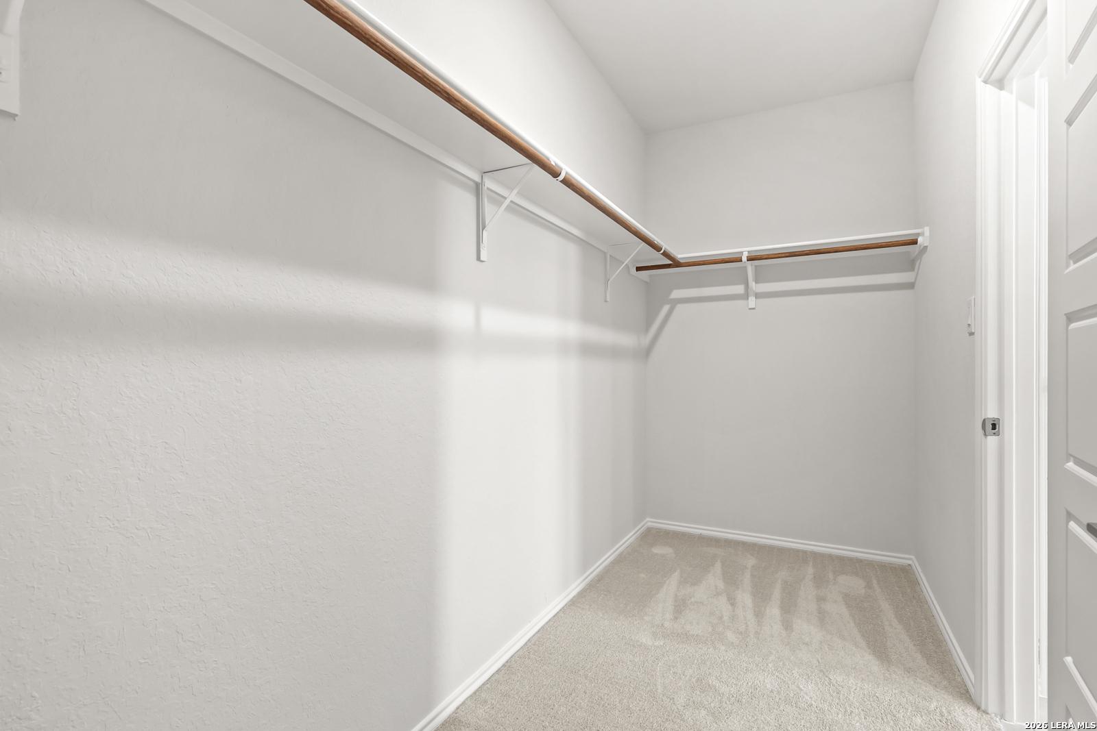 Spacious walk-in closet with wooden hanging rods and carpet flooring in Davidson Homes The Daphne I, Bricewood, San Antonio, Texas
