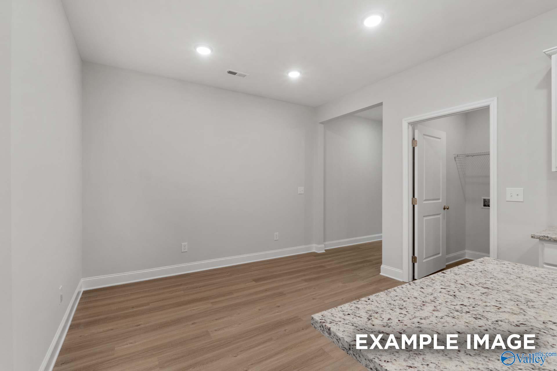 Modern kitchen with granite island, wood floors, and adjacent laundry in Davidson Homes The Camilla C, Hartselle, AL