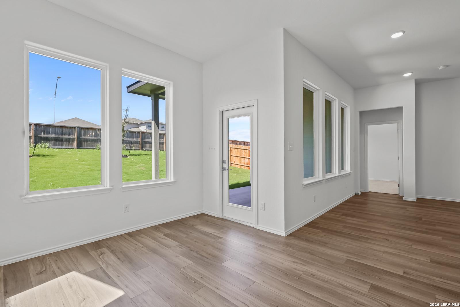 Sunlit living room with large windows, hardwood floors, and patio door overlooking green backyard in Davidson Homes The Sequoia B, San Antonio